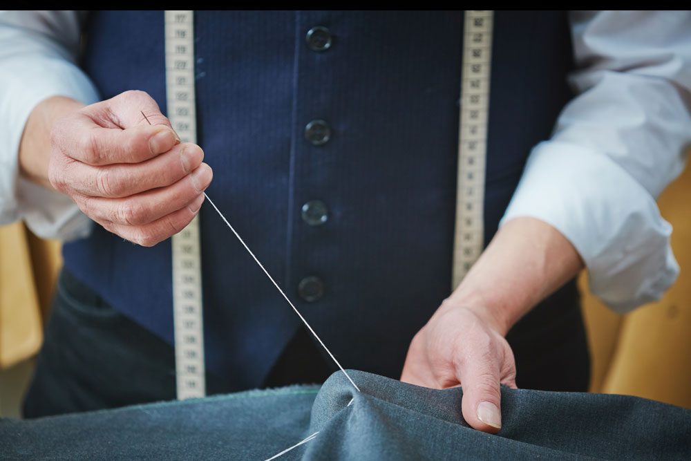 Tailor hand-stitching a seam with a tape measure around the neck